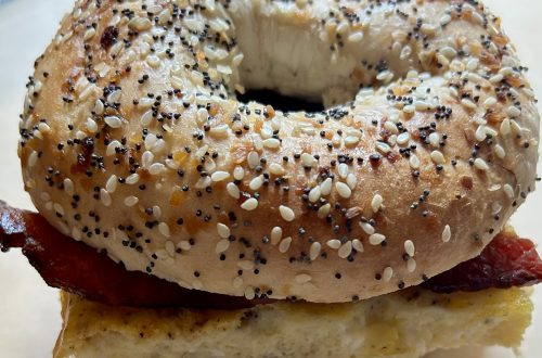 Lara"s homemade batch-cooked breakfast sandwich on an everything bagel with crispy bacon and fluffy eggs, wrapped in parchment paper for easy meal prepping.